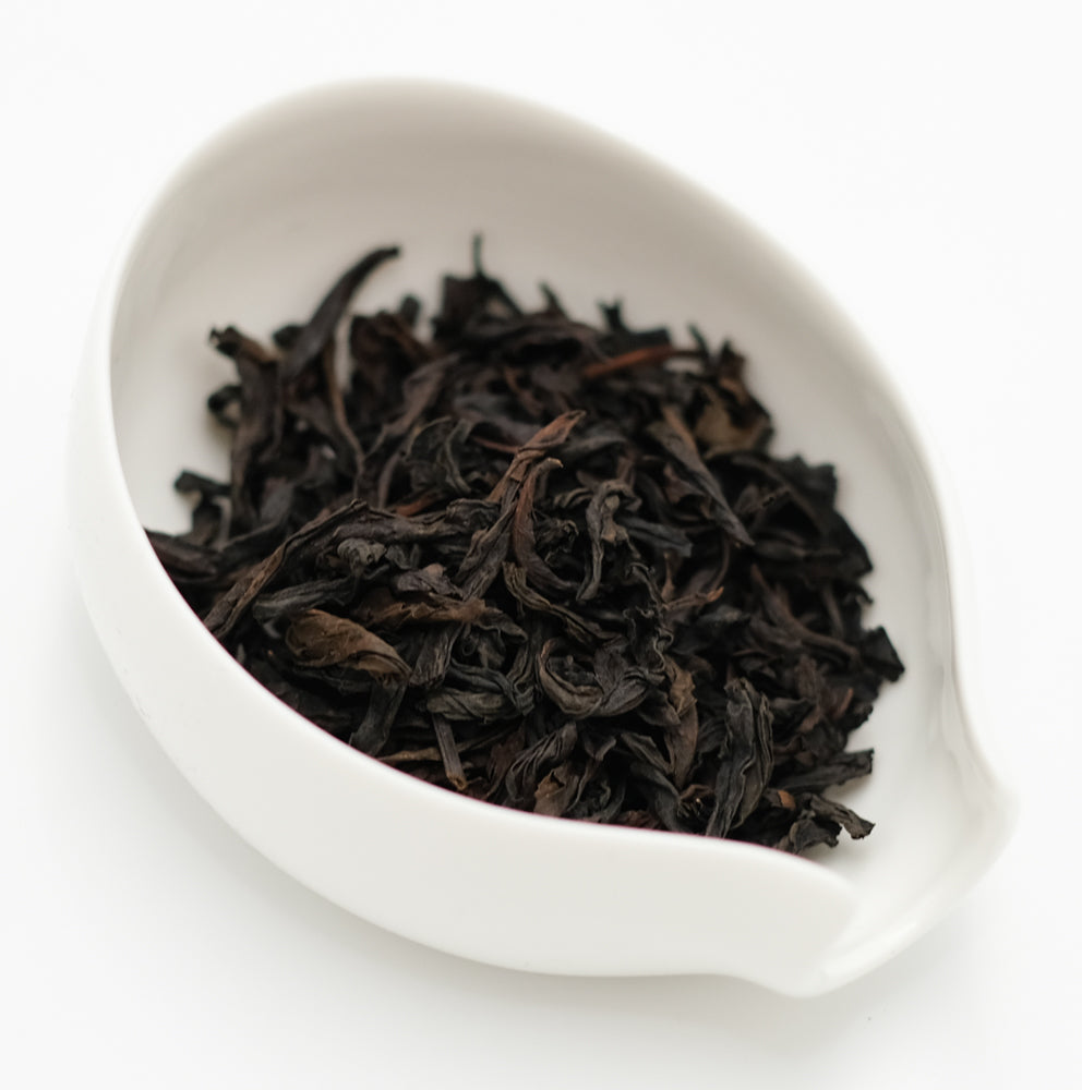 Dark, twisted Top Grade Rou Gui rock tea leaves heaped in a white porcelain scoop